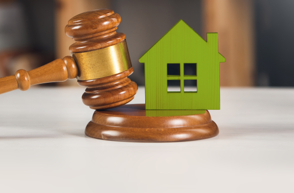 Richterhammer neben einem grünen Haus, symbolisiert rechtliche Aspekte in der Immobilienwirtschaft.