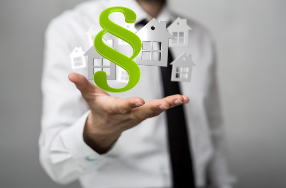 Hand mit Paragraphensymbol und stilisierten Häusern, passend zum Thema Hausgeld und Rechtsprechung.