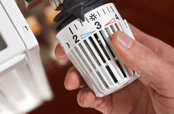 Hand dreht den Heizkörperregler, um Heizkosten und CO₂-Kosten effizient zu steuern.