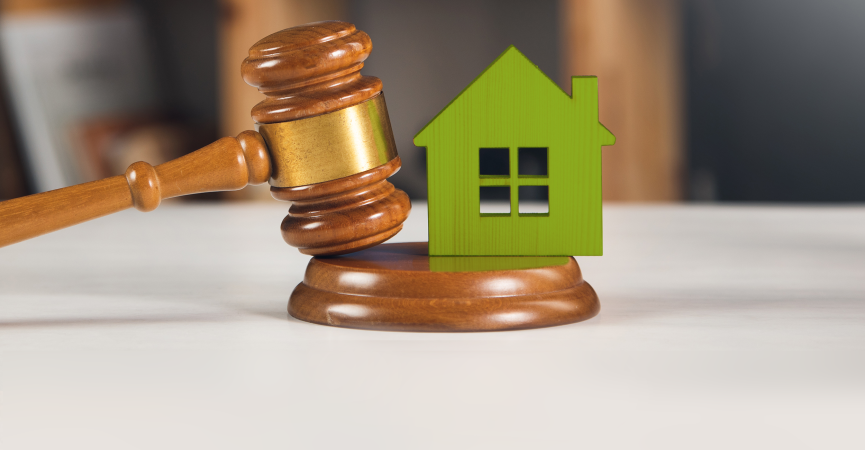 Richterhammer neben einem grünen Haus, symbolisiert rechtliche Aspekte in der Immobilienwirtschaft.